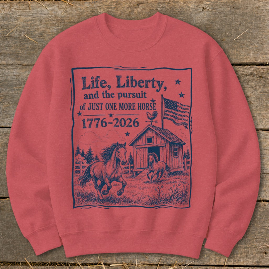 Crewneck sweatshirt with dark blue graphic of horses, barn, US flag, and text "Life, Liberty, and the pursuit of JUST ONE MORE HORSE 1776-2026".