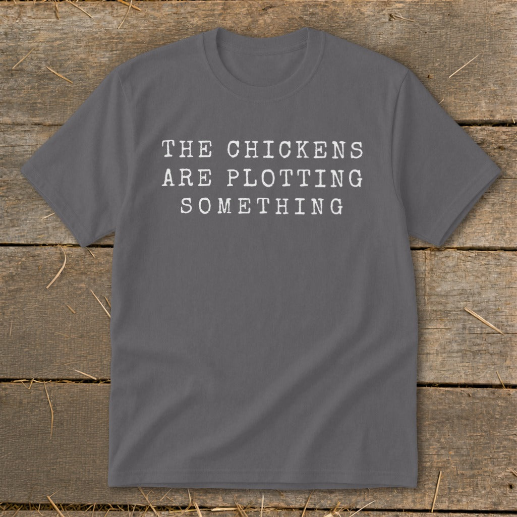 Grey t-shirt with white text reading "The chickens are plotting something."