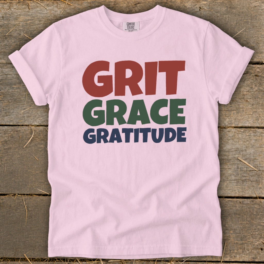 Light pink t-shirt featuring the stacked text GRIT, GRACE, and GRATITUDE in red, green, and blue.