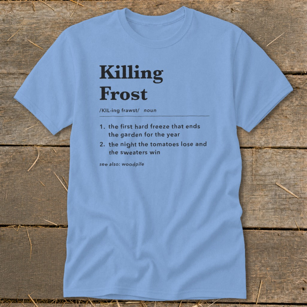A light blue t-shirt printed with a dictionary definition of Killing Frost lies flat on a wooden surface.
