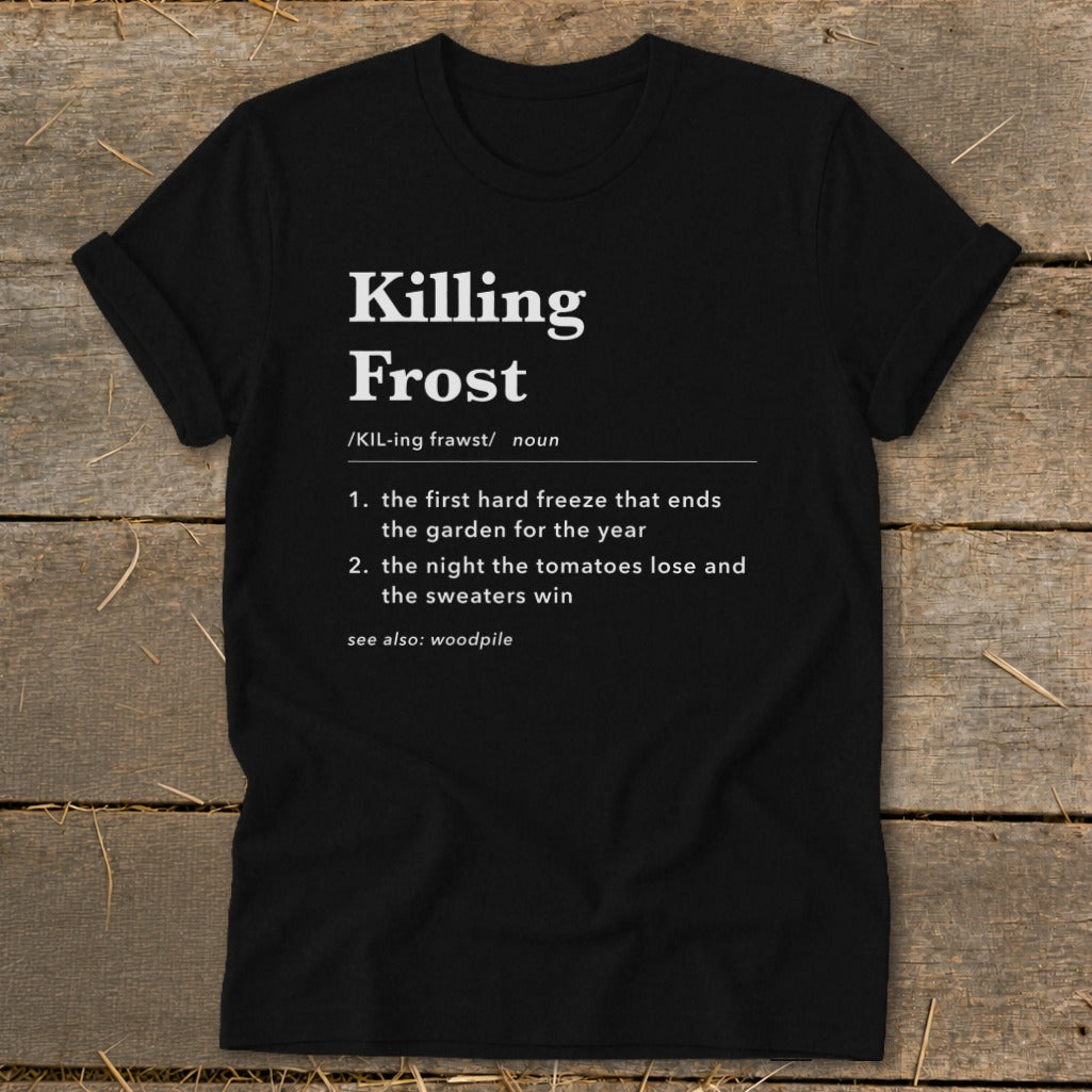 Black t-shirt featuring dictionary definition text for Killing Frost, laid flat on a rustic wooden surface.