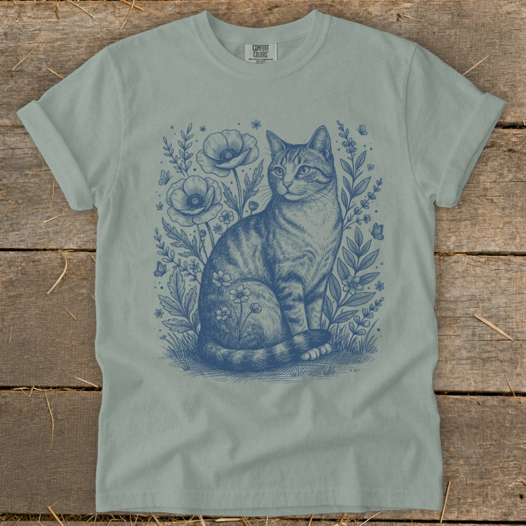 T-shirt with blue sketch of a tabby cat sitting among wildflowers and butterflies.