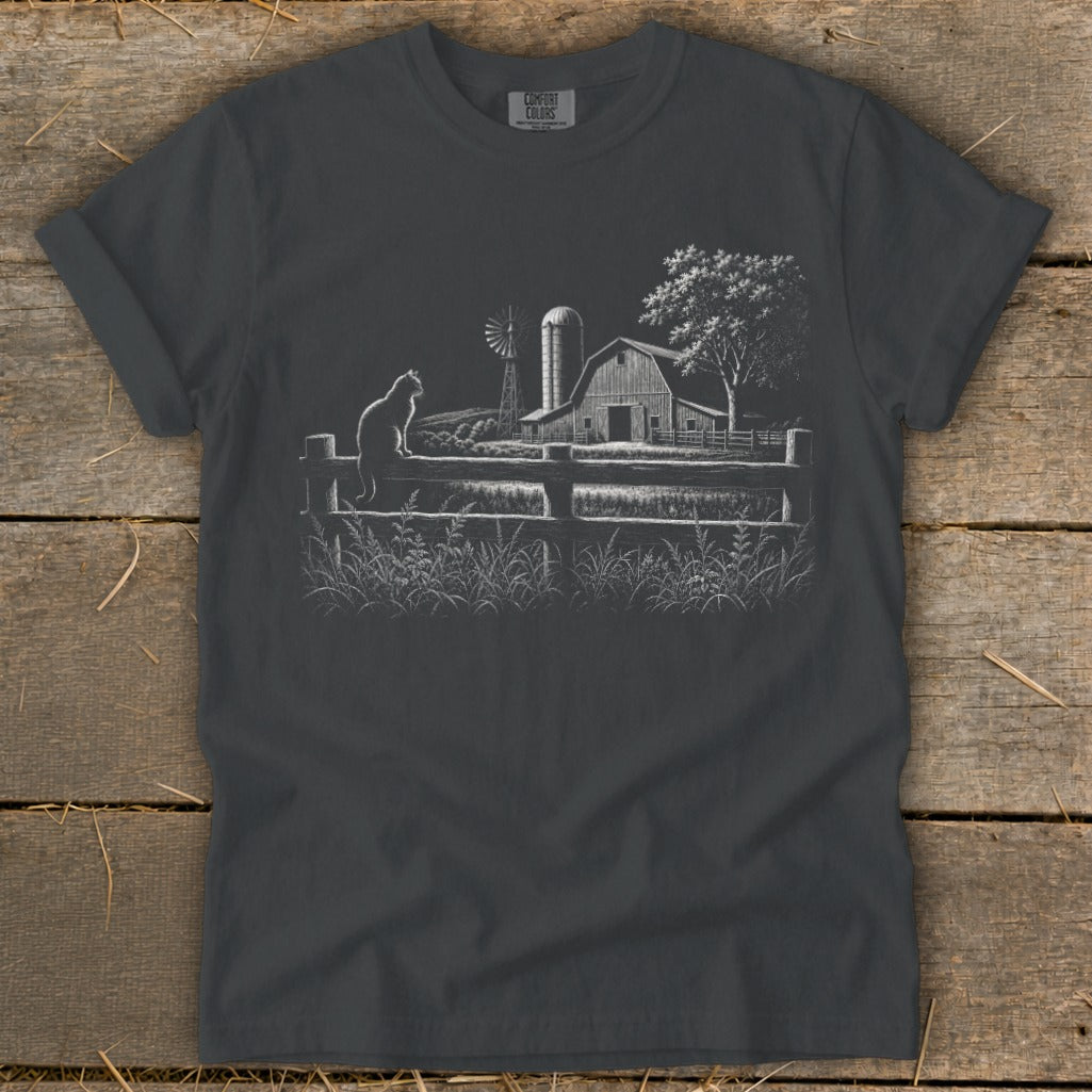Cat sitting on a wooden fence with a barn and windmill in the background.