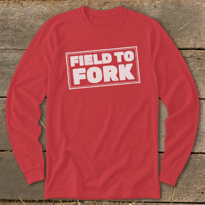 A red long-sleeve t-shirt with a white stamped box design reading Field to Fork on a wooden background.