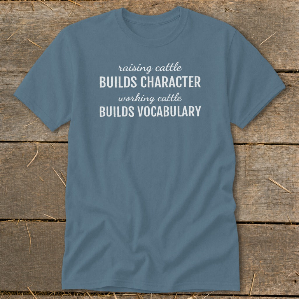 Blue t-shirt with white text: "raising cattle BUILDS CHARACTER working cattle BUILDS VOCABULARY".