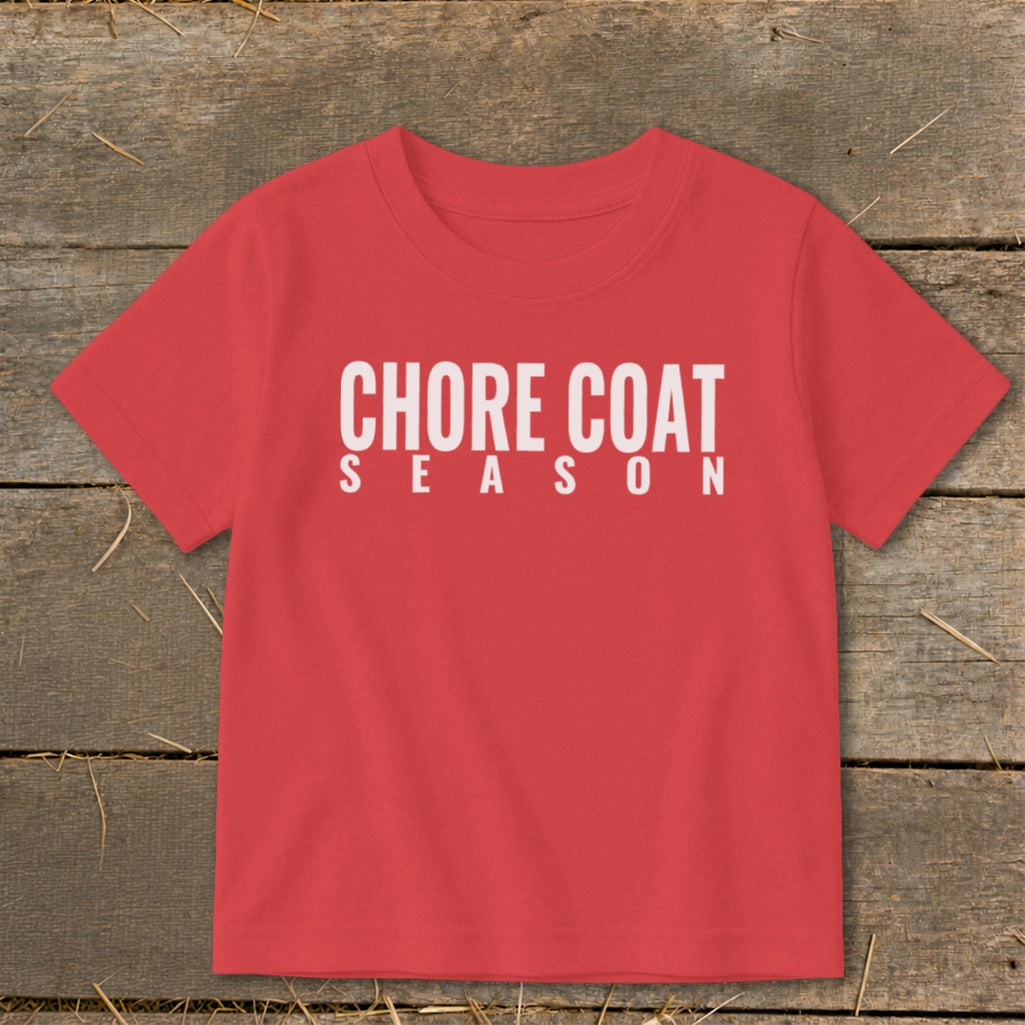 Red t-shirt with white text "CHORE COAT SEASON" on a wooden background.