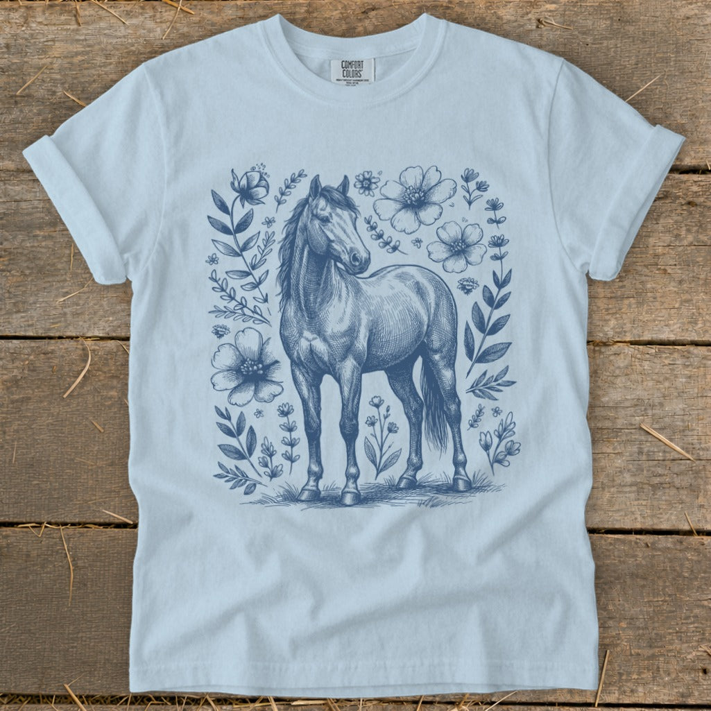 Light blue t-shirt with sketch of a horse surrounded by flowers and leaves.