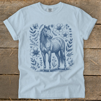 Light blue t-shirt with sketch of a horse surrounded by flowers and leaves.