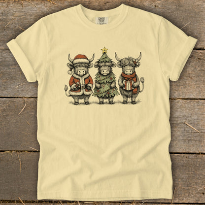 Three highland cows in festive holiday attire, one dressed as Santa, one as a Christmas tree, and one holding a gift.
