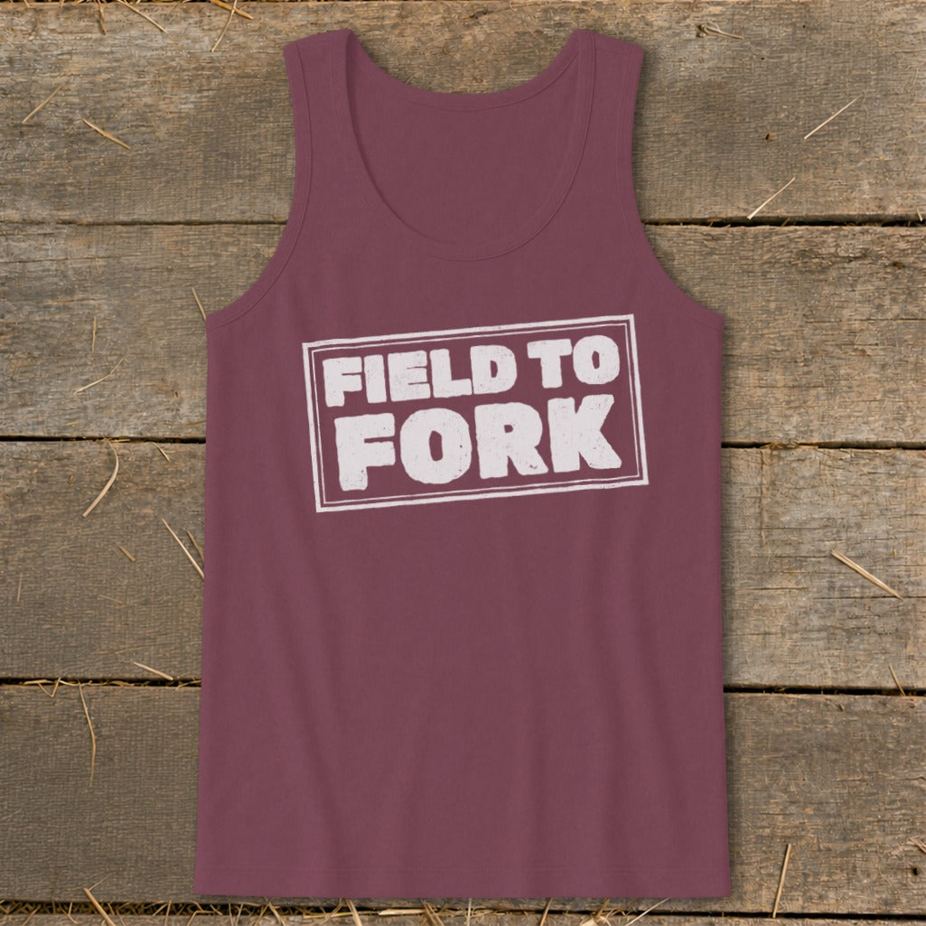 Maroon tank top featuring the white text Field to Fork inside a bordered rectangle, laid flat on a rustic wooden surface.