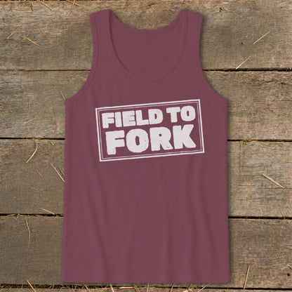 Maroon tank top featuring the white text Field to Fork inside a bordered rectangle, laid flat on a rustic wooden surface.