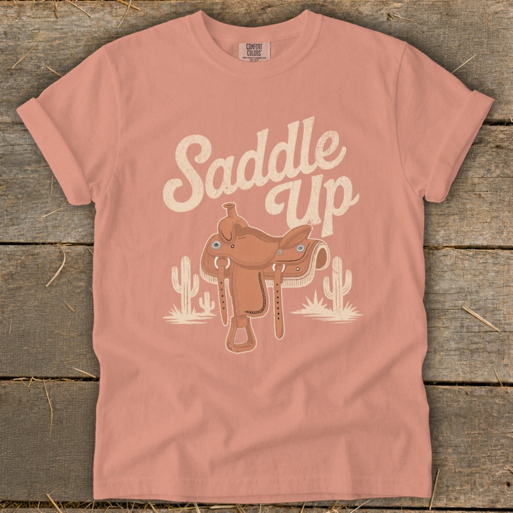 Pink t-shirt with "Saddle Up" text and cowboy saddle graphic with cacti.