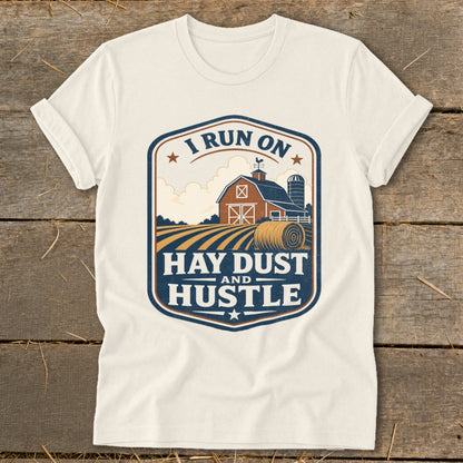 Cream t-shirt with "I Run On Hay Dust And Hustle" farm graphic.