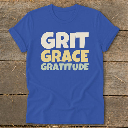 Royal blue crewneck t-shirt with rolled sleeves laid flat on wood, featuring the text GRIT GRACE GRATITUDE.