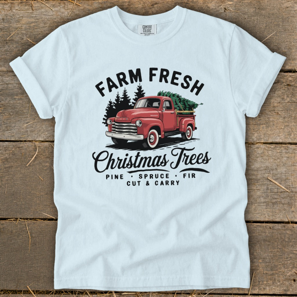 Light blue t-shirt with red truck carrying Christmas trees, text reads "Farm Fresh Christmas Trees".