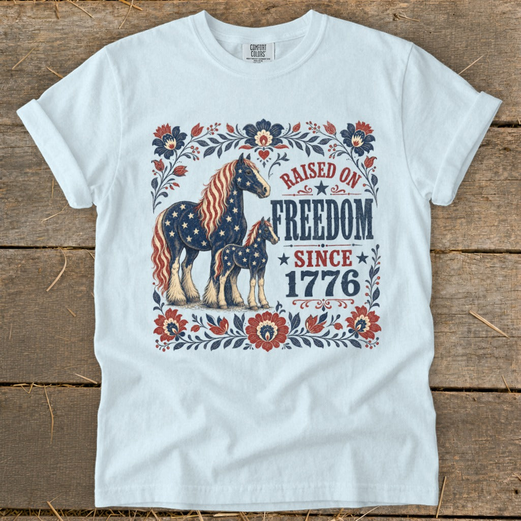 White t-shirt with patriotic horses and "Raised on Freedom Since 1776" text.