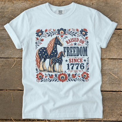 White t-shirt with patriotic horses and "Raised on Freedom Since 1776" text.