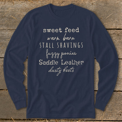 Navy long sleeve shirt with text: sweet feed, warm barn, stall shavings, fuzzy ponies, saddle leather, dusty boots.