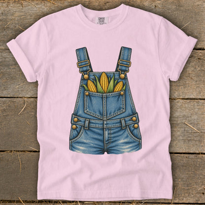 Pink t-shirt with a denim overalls graphic featuring corn in the pocket.