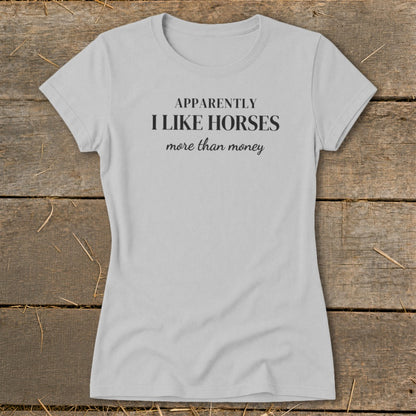 Light grey t-shirt with black text that reads "APPARENTLY I LIKE HORSES more than money".