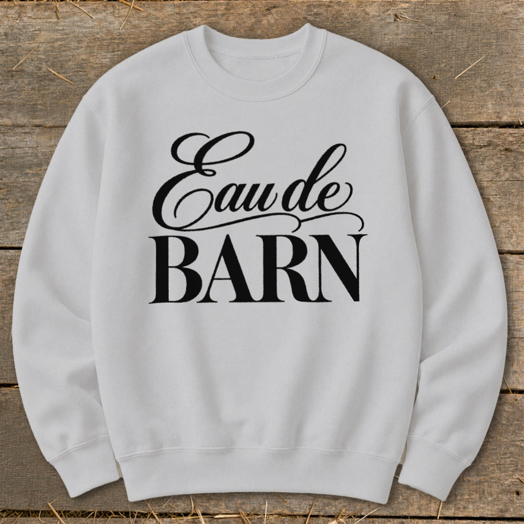 White sweatshirt with black text reading "Eau de BARN" on a wooden background.
