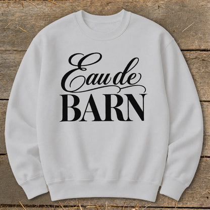 White sweatshirt with black text reading "Eau de BARN" on a wooden background.