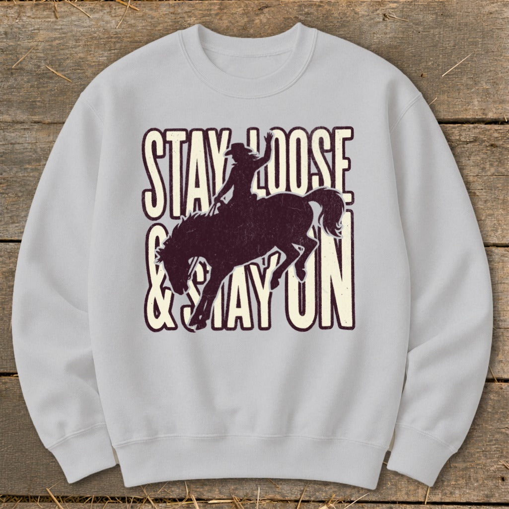 Light gray sweatshirt with a bronco rider graphic and text "STAY LOOSE & STAY ON".