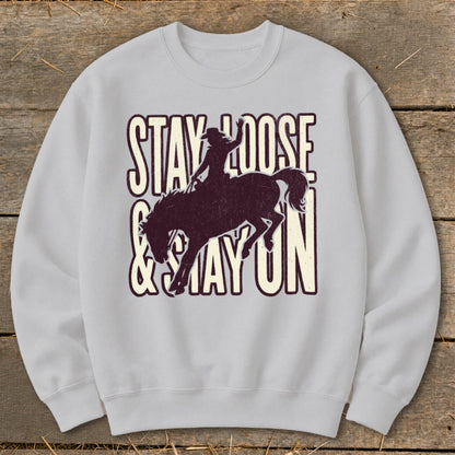 Light gray sweatshirt with a bronco rider graphic and text "STAY LOOSE & STAY ON".
