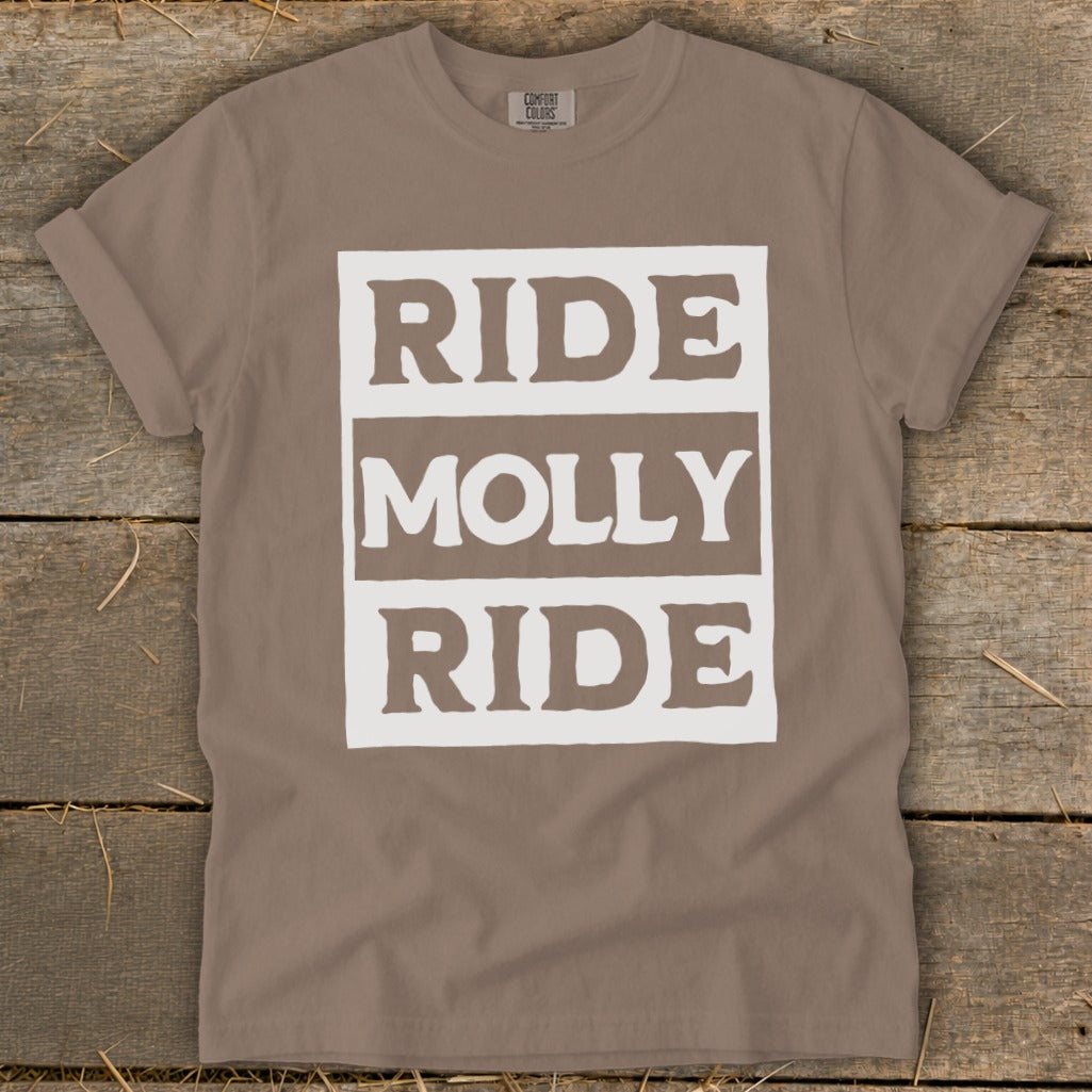 Brown t-shirt with rolled sleeves featuring a white graphic block reading RIDE MOLLY RIDE laid flat on wood.