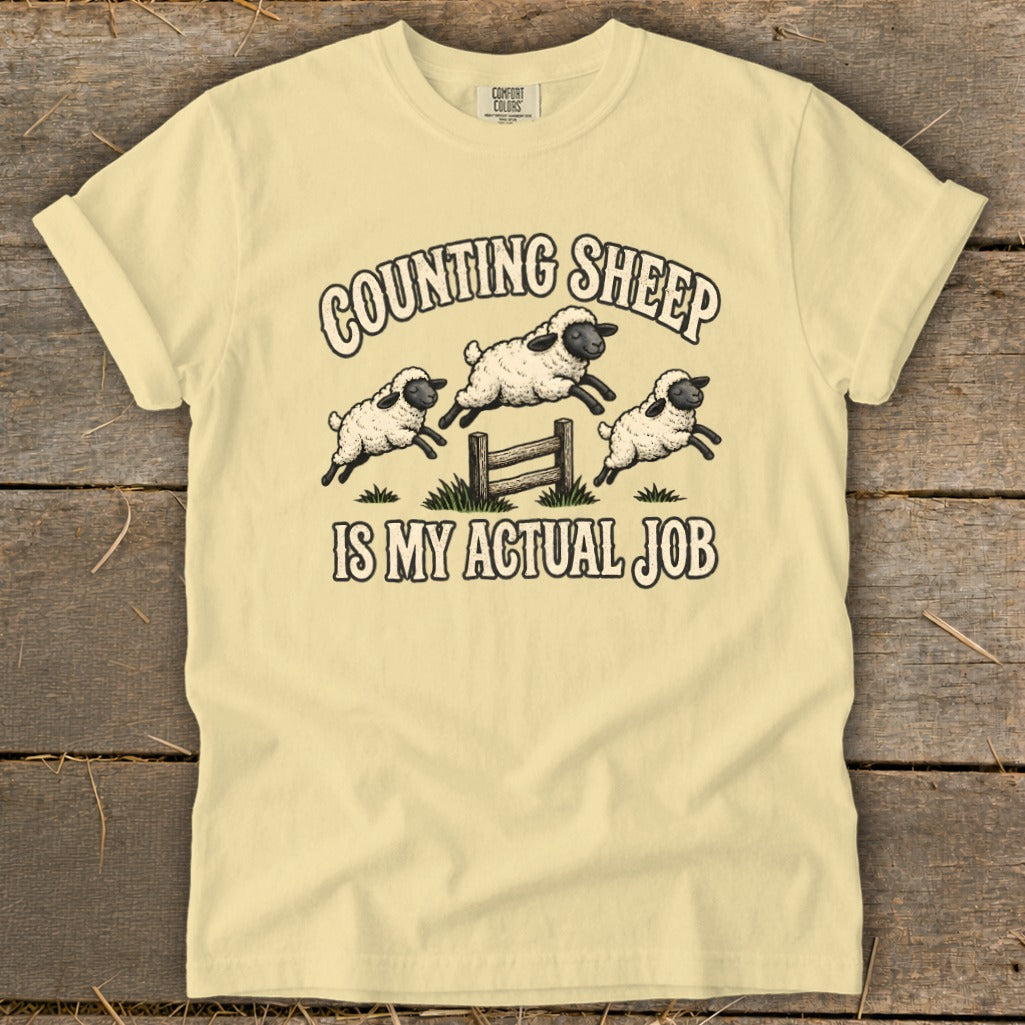 Yellow t-shirt with sheep jumping over a fence, text "Counting Sheep Is My Actual Job".