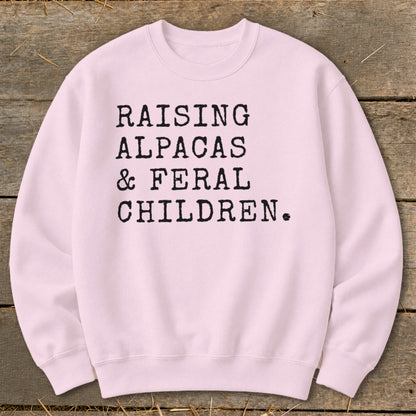 Pink sweatshirt with black text: "RAISING ALPACAS & FERAL CHILDREN."