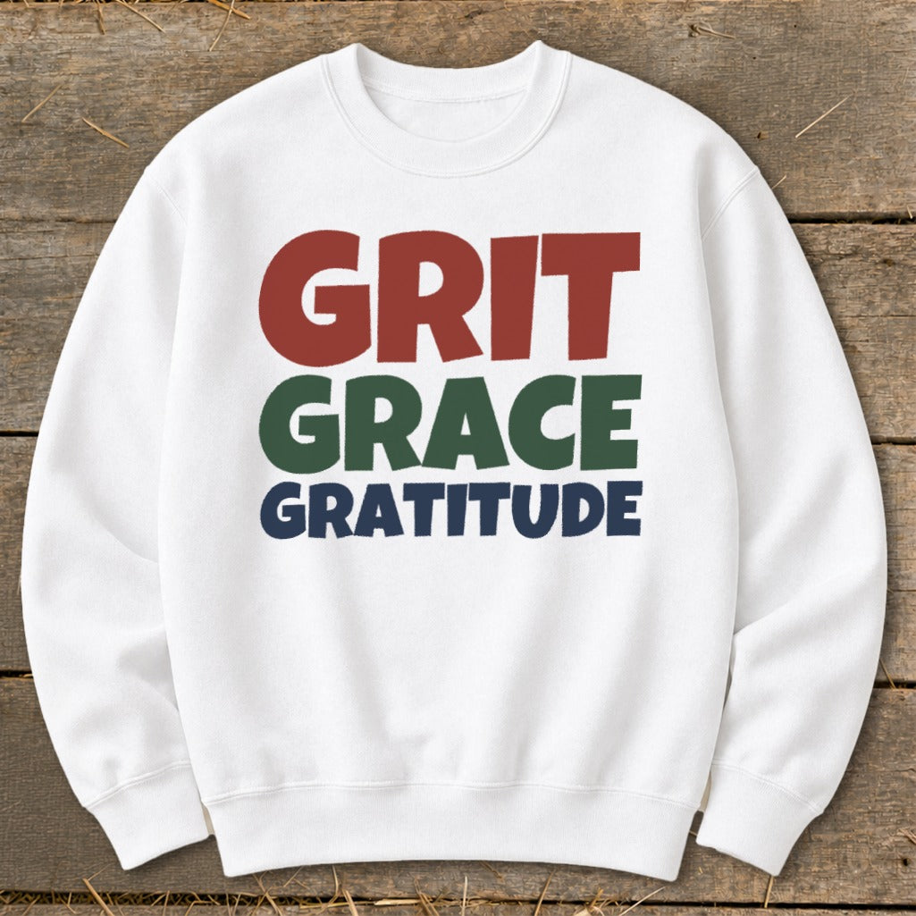 A white crewneck sweatshirt featuring the words GRIT in red, GRACE in green, and GRATITUDE in blue.