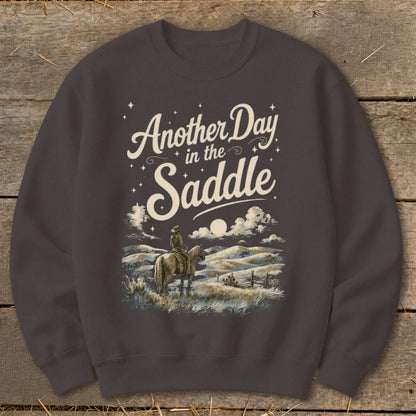 Graphic on sweatshirt with text "Another Day in the Saddle" and a cowboy on horseback.