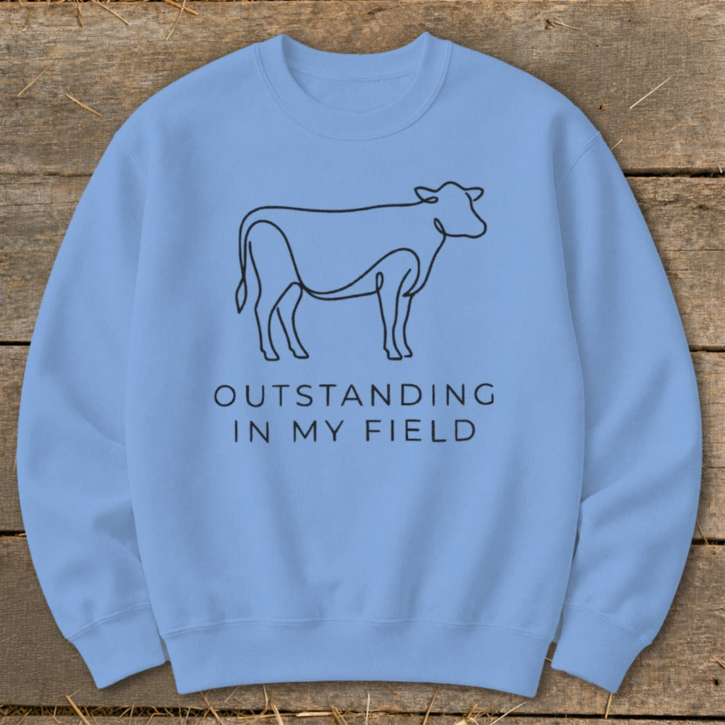 Light blue sweatshirt with line drawing of a cow and text "OUTSTANDING IN MY FIELD".