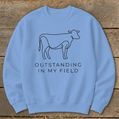 Light blue sweatshirt with line drawing of a cow and text "OUTSTANDING IN MY FIELD".
