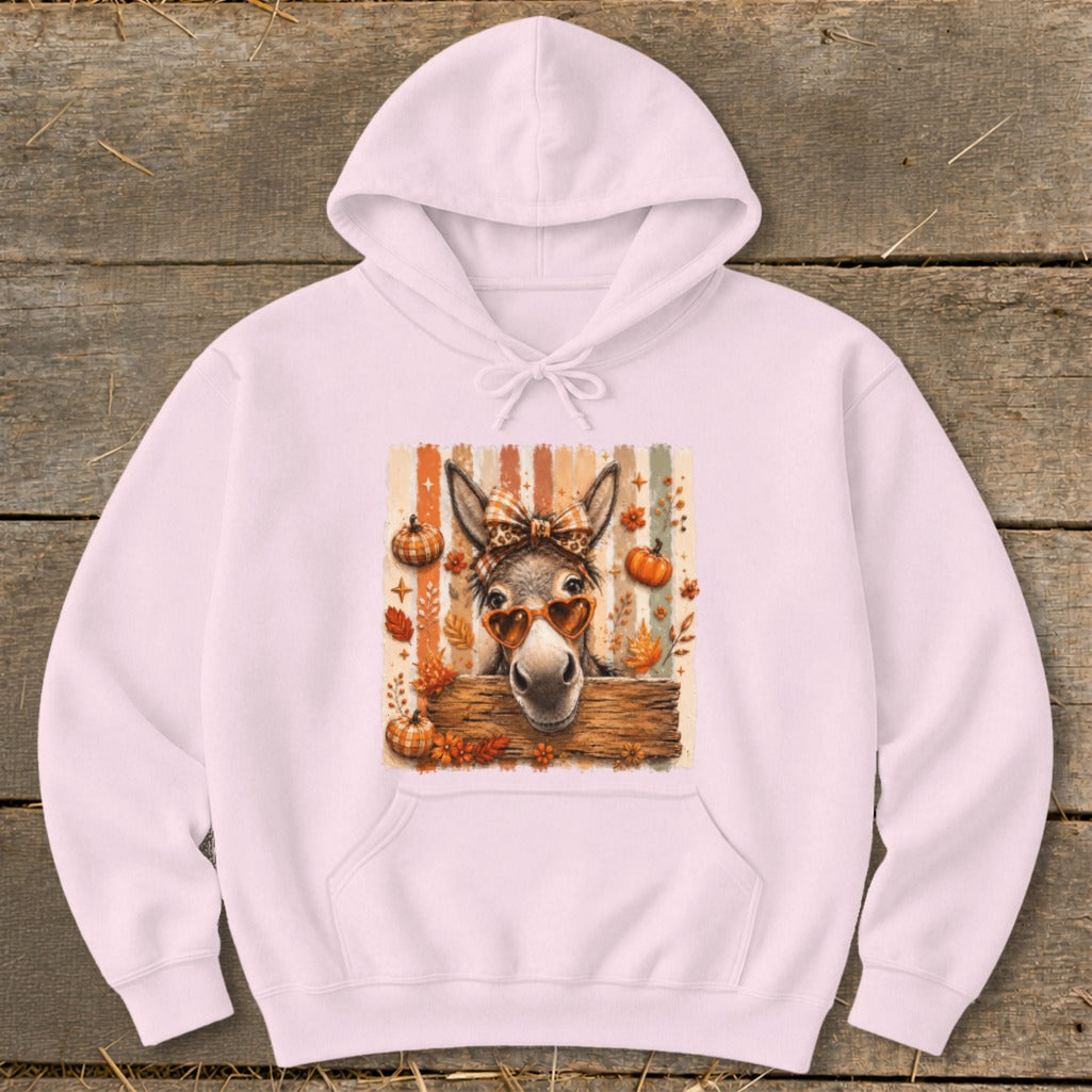 Pink hoodie with a donkey wearing heart sunglasses and a bow, surrounded by fall leaves and pumpkins.