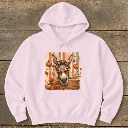Pink hoodie with a donkey wearing heart sunglasses and a bow, surrounded by fall leaves and pumpkins.