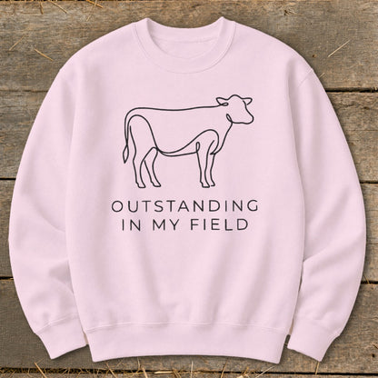 Pink crewneck sweatshirt with line drawing of a cow and text "OUTSTANDING IN MY FIELD".
