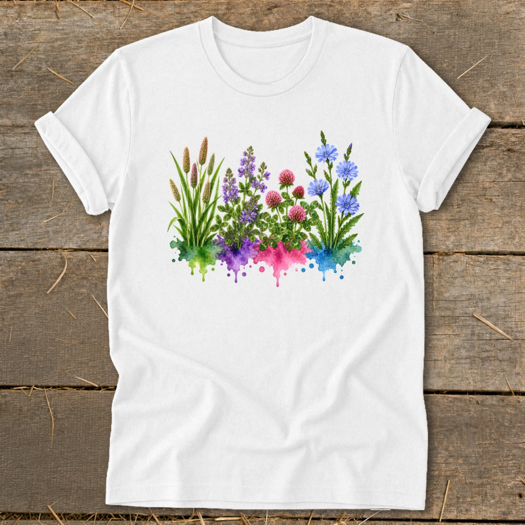 A white crewneck t-shirt lies flat on a wooden surface, featuring a colorful watercolor wildflower graphic on the chest.