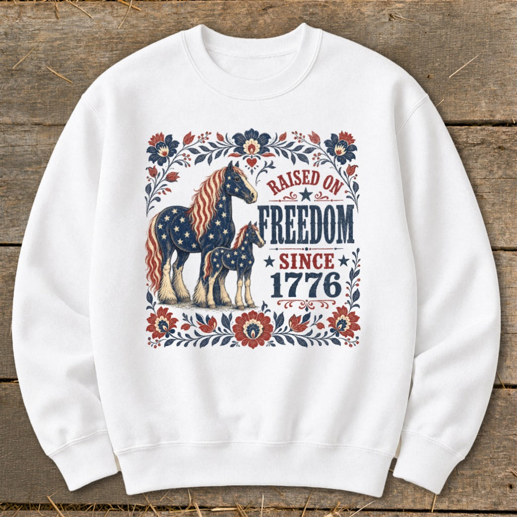White sweatshirt with American flag-themed horses and "Raised on Freedom Since 1776" text.