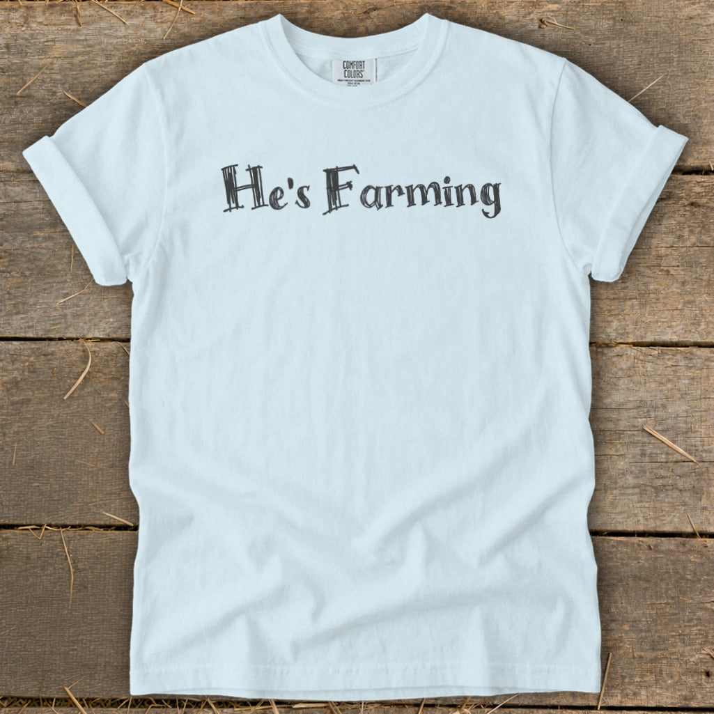 Light blue t-shirt with "He's Farming" printed in black distressed font.