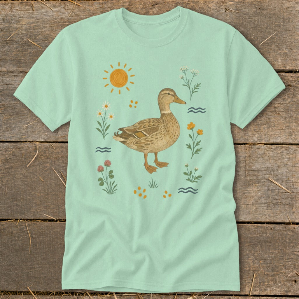 Mint t-shirt with a watercolor illustration of a duck surrounded by flowers, sun, and water.