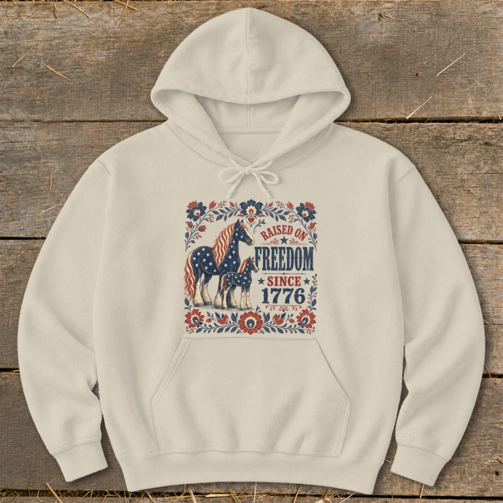 Cream hoodie with horses and "Raised on Freedom Since 1776" patriotic graphic.