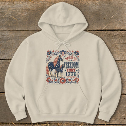 Cream hoodie with horses and "Raised on Freedom Since 1776" patriotic graphic.