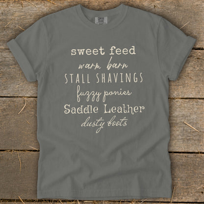 Gray t-shirt with "sweet feed warm barn stall shavings fuzzy ponies saddle leather dusty boots" text.