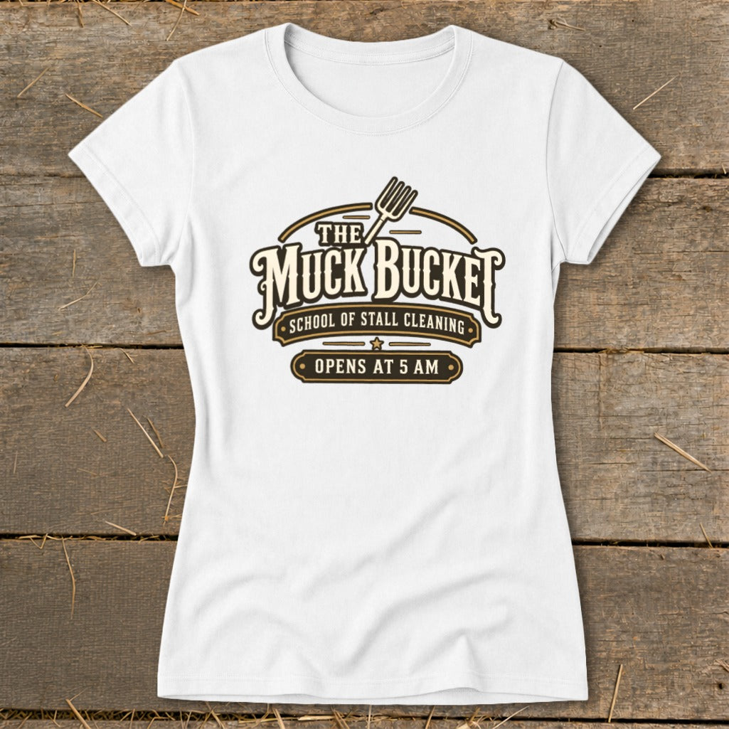 White t-shirt with "The Muck Bucket" logo, "School of Stall Cleaning", and "Opens at 5 AM".