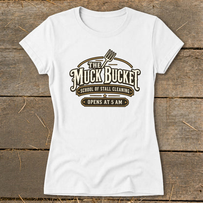 White t-shirt with "The Muck Bucket" logo, "School of Stall Cleaning", and "Opens at 5 AM".