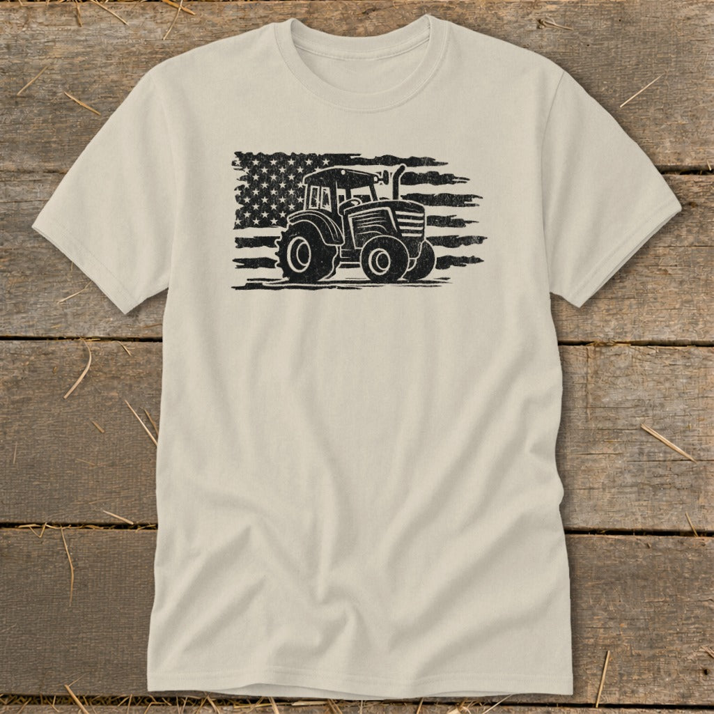 Tractor graphic superimposed on a distressed American flag design on a beige t-shirt.