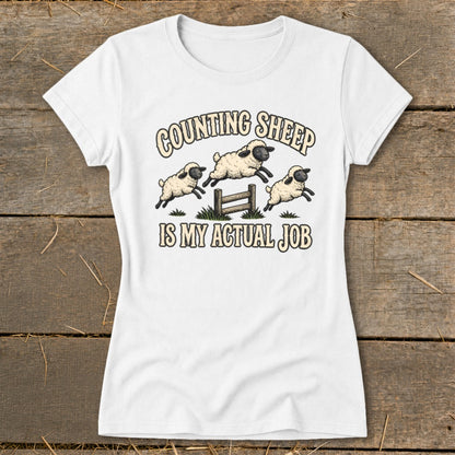 White t-shirt with graphic of sheep jumping over a fence, text reads "COUNTING SHEEP IS MY ACTUAL JOB".