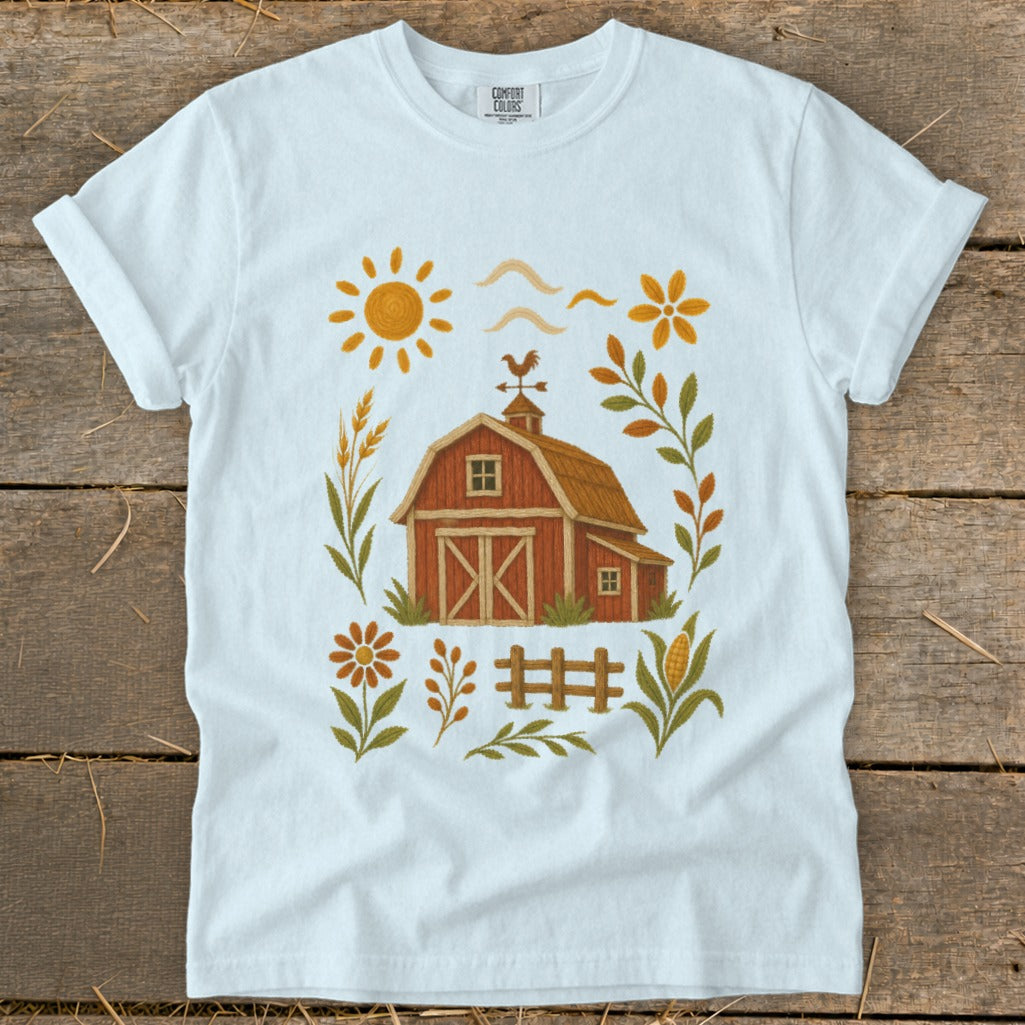 White t-shirt with a rustic farm scene featuring a barn, sun, and floral elements.